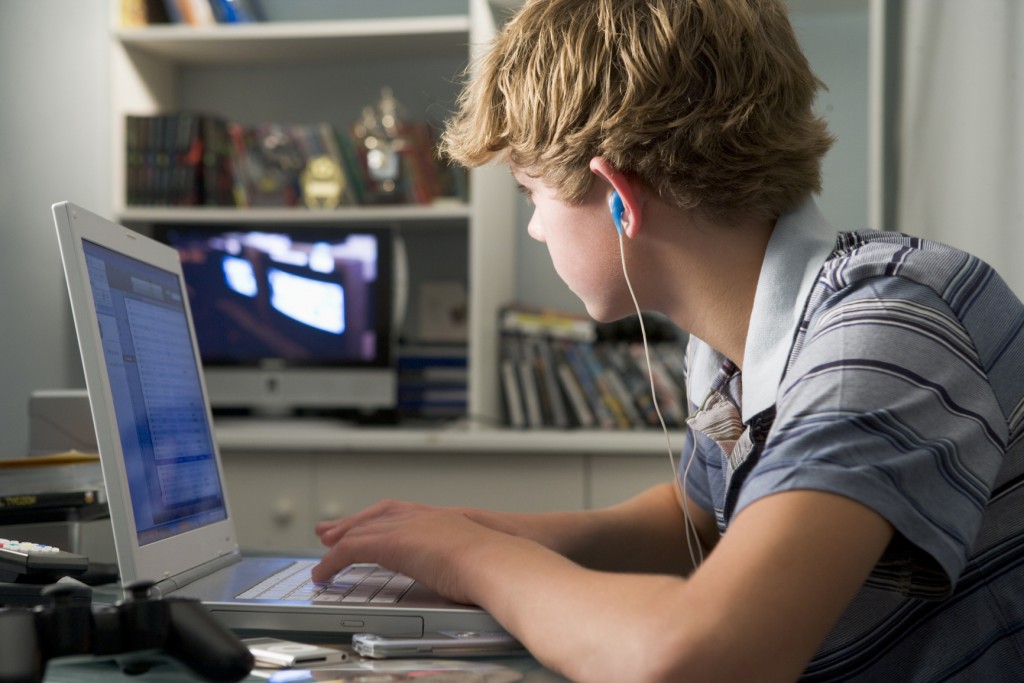 Young boy in bedroom using laptop and listening to MP3 player